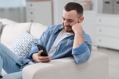 Smiling man with smartphone on sofa at home