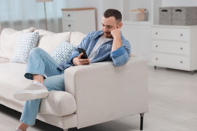 Handsome man using smartphone on sofa indoors