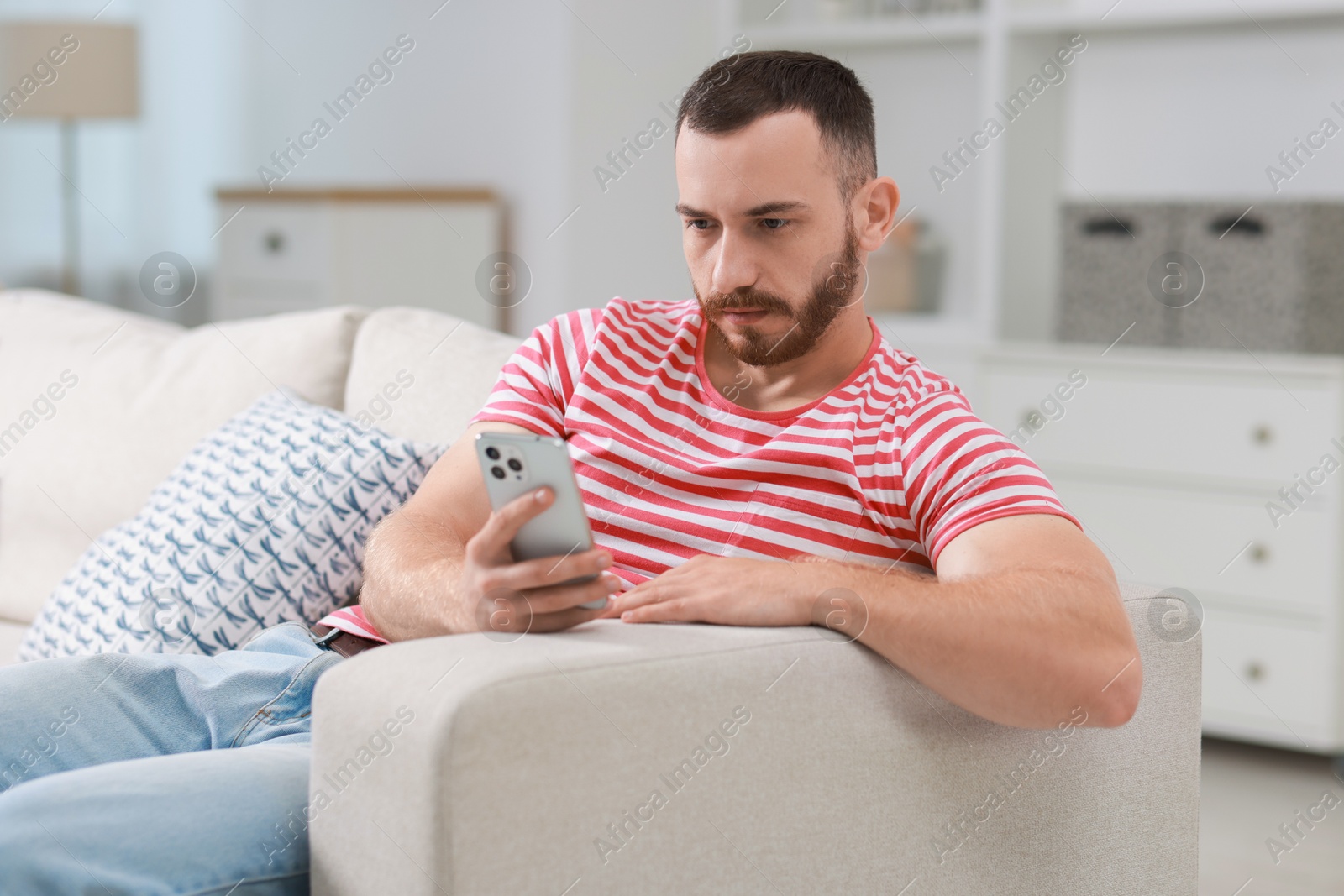 Photo of Handsome man using smartphone on sofa indoors