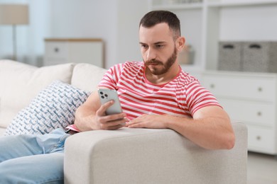 Photo of Handsome man using smartphone on sofa indoors