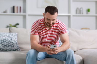 Photo of Handsome man using smartphone on sofa indoors