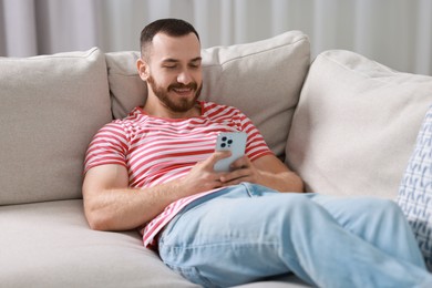 Happy man using smartphone on sofa indoors