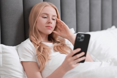 Beautiful woman looking at smartphone in bed