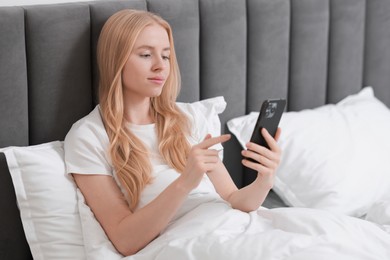 Beautiful woman looking at smartphone in bed