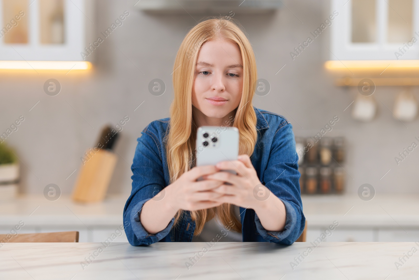 Photo of Beautiful woman using smartphone at white table in kitchen