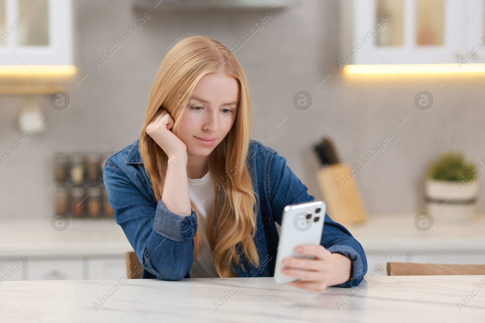 Photo of Beautiful woman using smartphone at white table in kitchen