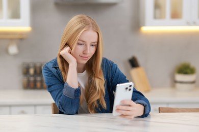 Beautiful woman using smartphone at white table in kitchen