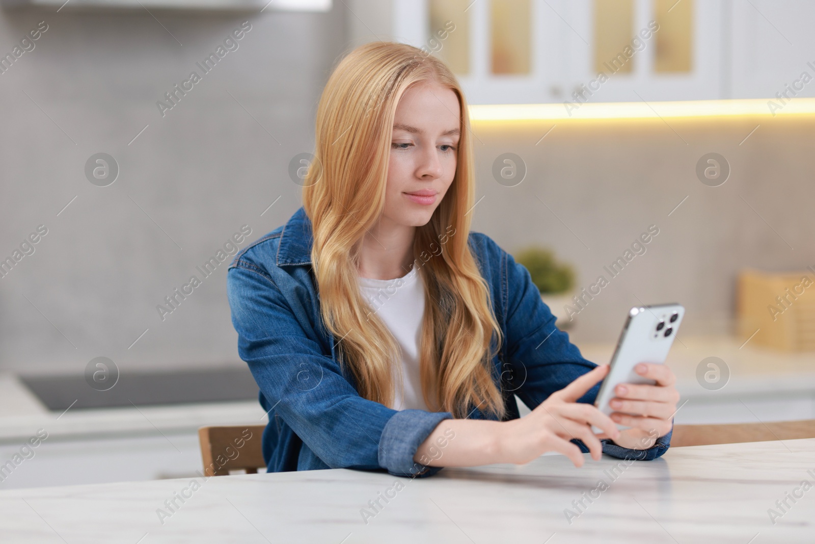 Photo of Beautiful woman using smartphone at white table in kitchen