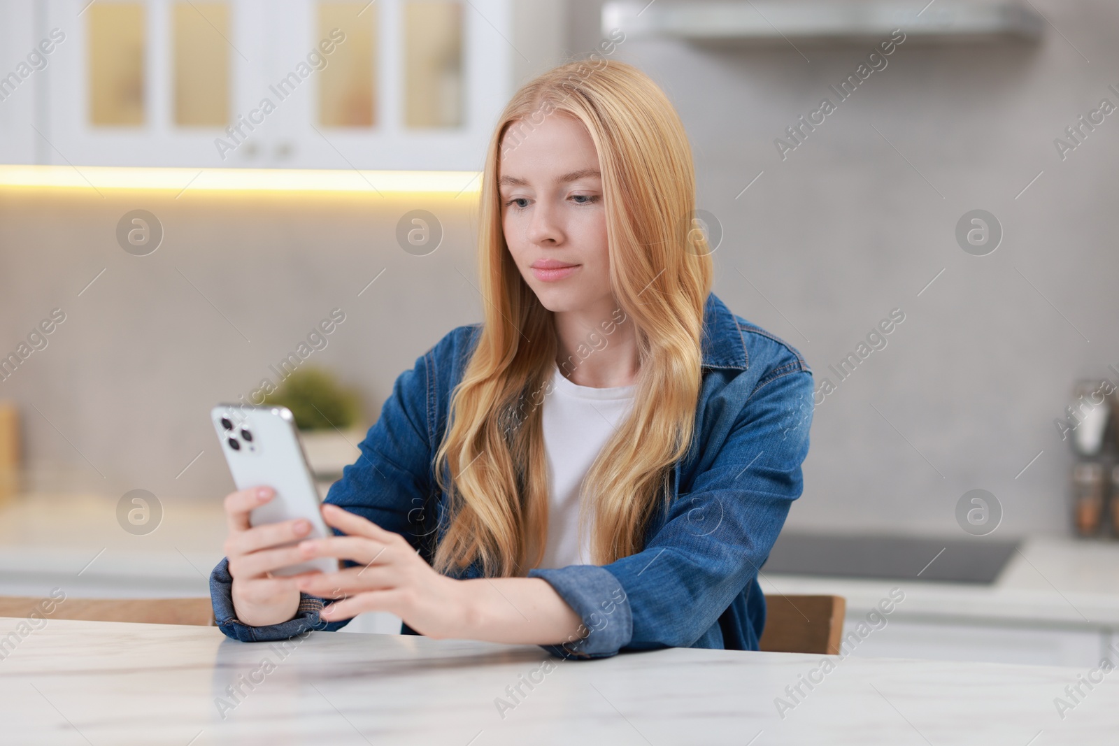 Photo of Beautiful woman using smartphone at white table in kitchen