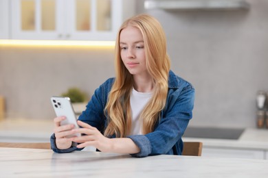 Beautiful woman using smartphone at white table in kitchen