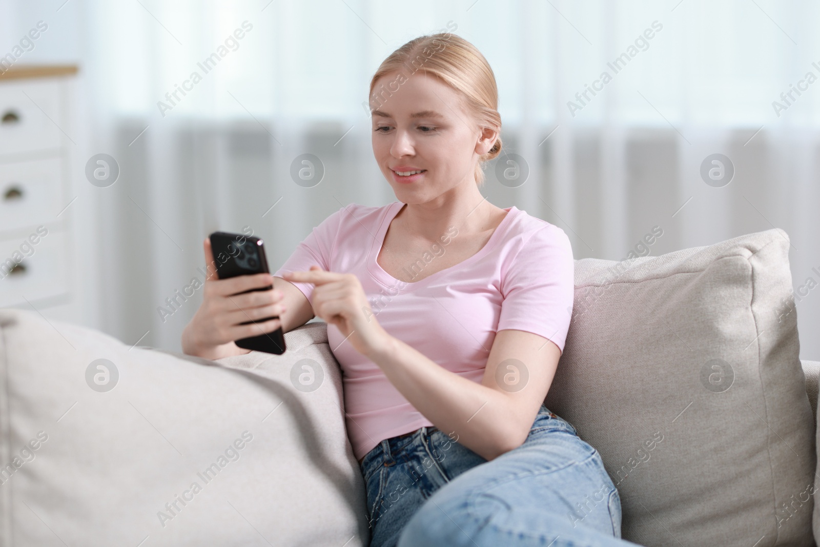 Photo of Smiling woman using smartphone on sofa indoors