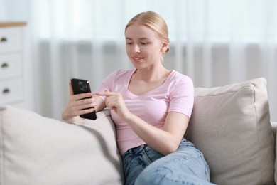 Smiling woman using smartphone on sofa indoors