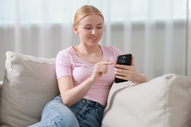 Photo of Smiling woman using smartphone on sofa indoors