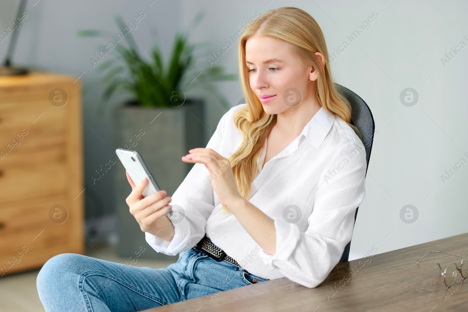 Photo of Beautiful woman using smartphone at table in office