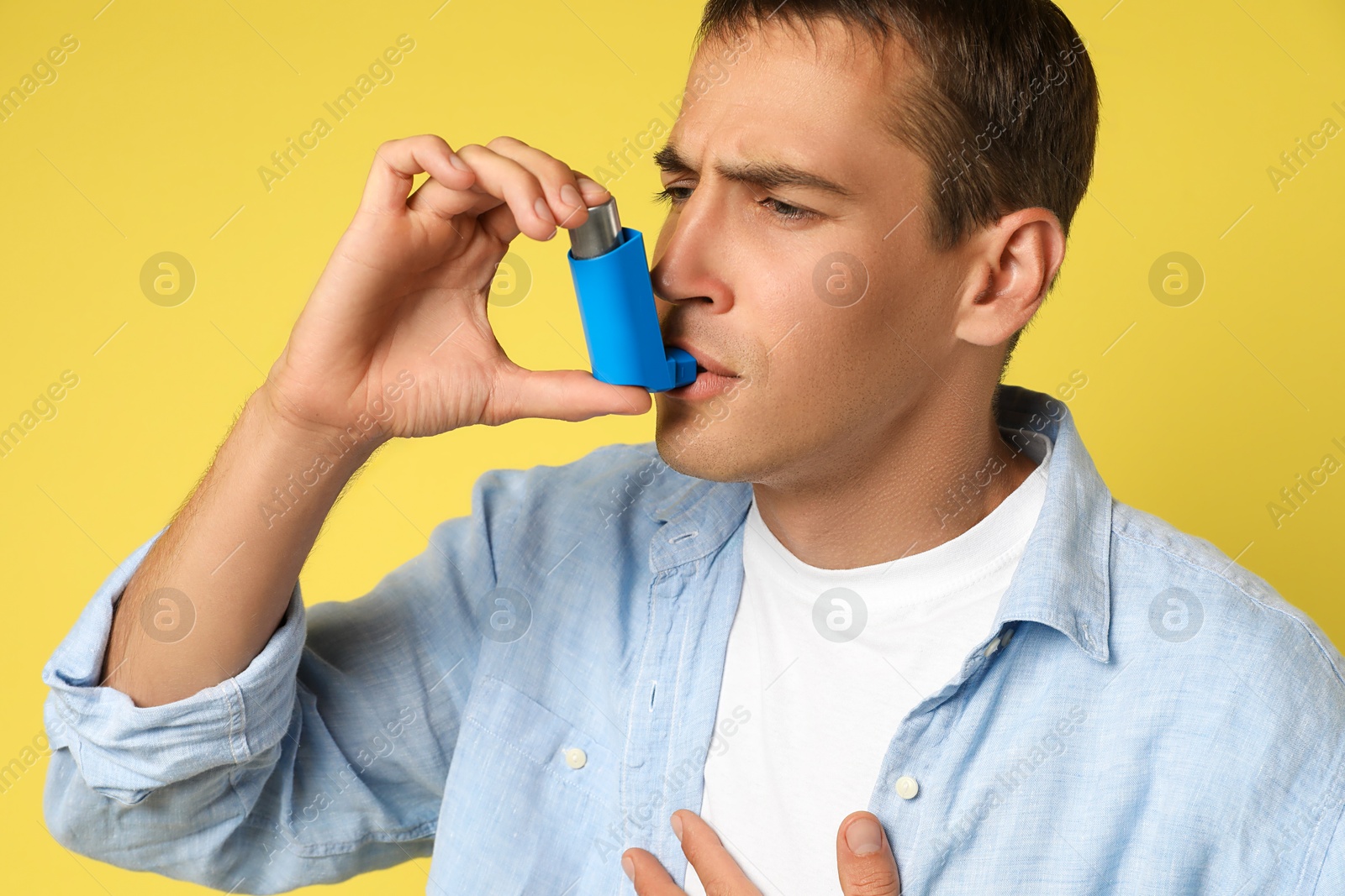 Photo of Man using asthma inhaler on yellow background