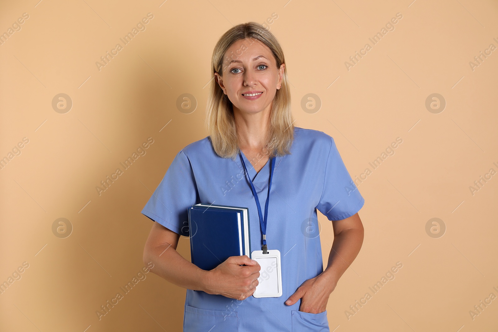 Photo of Nurse in medical uniform with badge and books on beige background