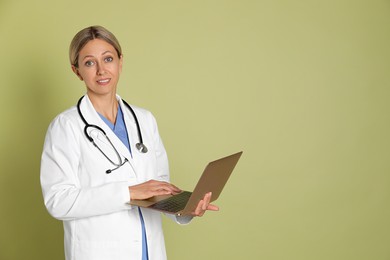 Doctor in medical uniform with stethoscope and laptop on light green background, space for text