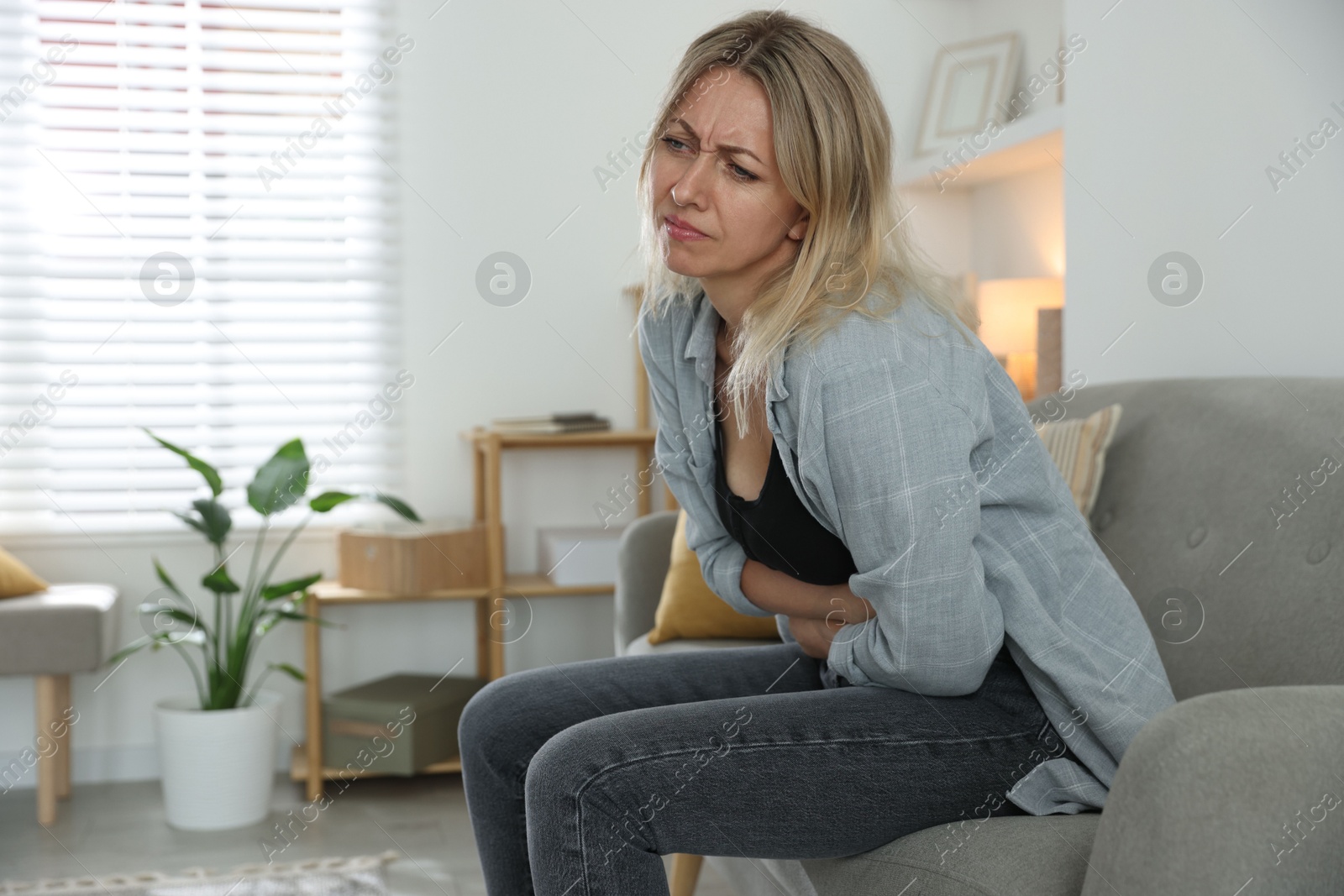 Photo of Menopause. Woman suffering from abdominal pain on sofa at home