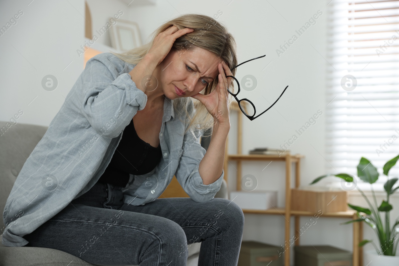 Photo of Menopause. Woman suffering from headache on sofa at home