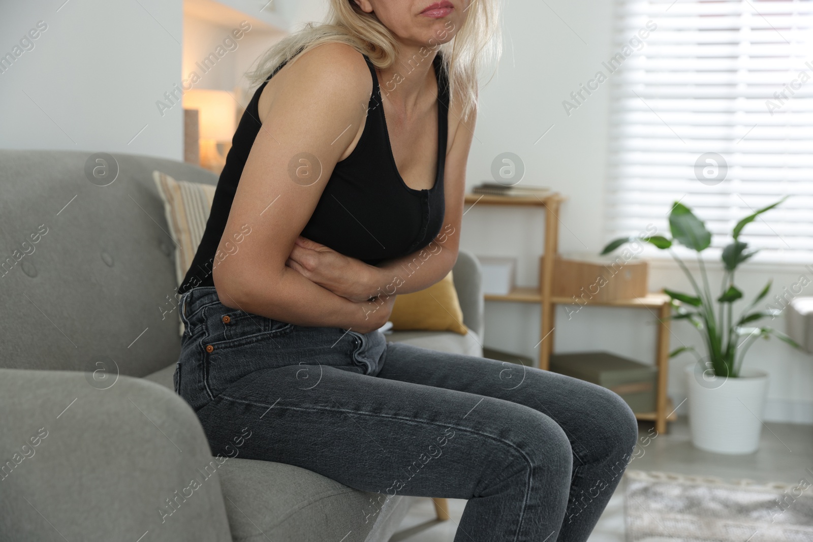 Photo of Menopause. Woman suffering from abdominal pain on sofa at home, closeup