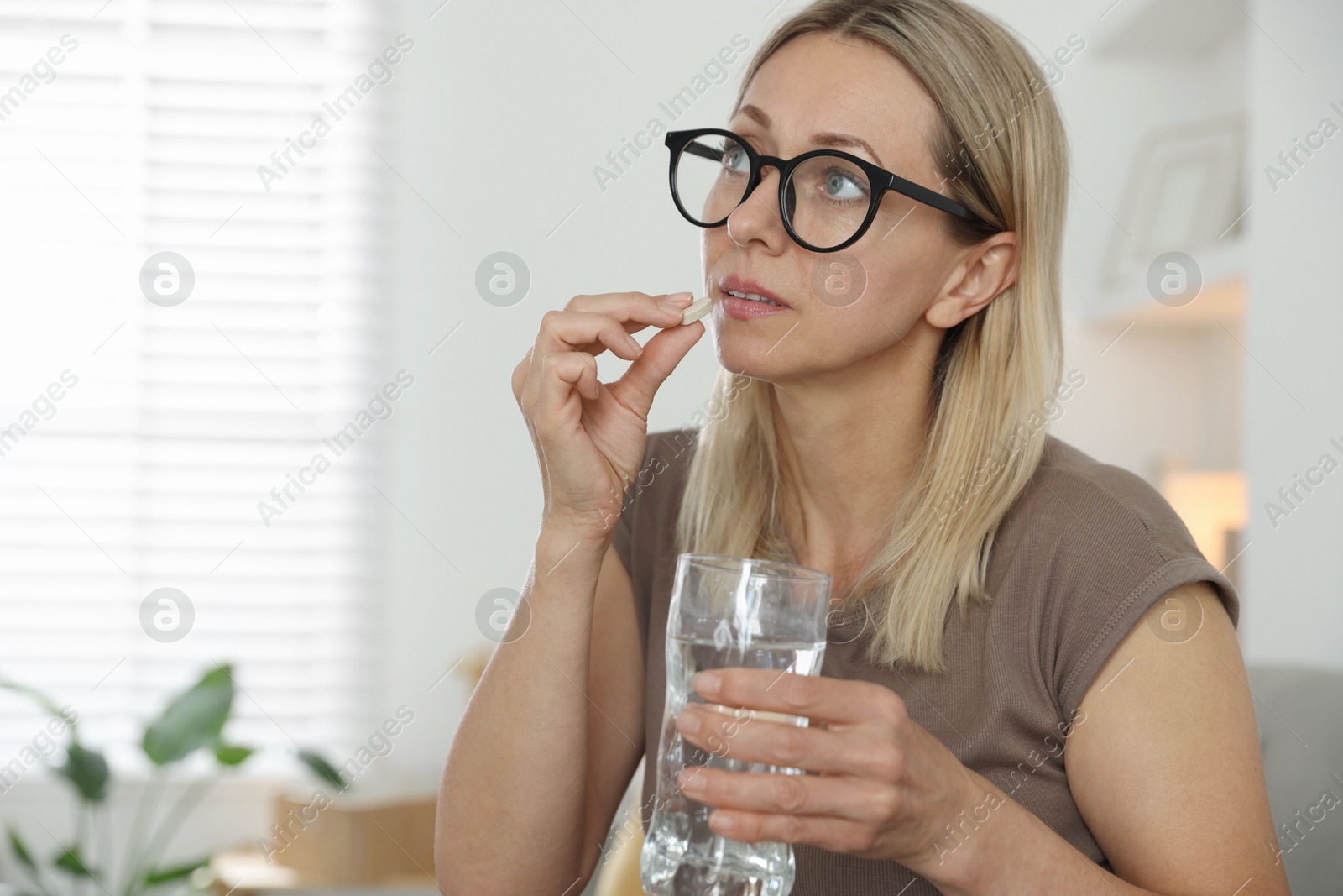 Photo of Menopause, hormone replacement therapy. Woman with glass of water taking pill at home, space for text