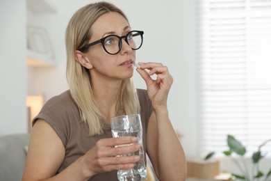 Photo of Menopause, hormone replacement therapy. Woman with glass of water taking pill at home, space for text