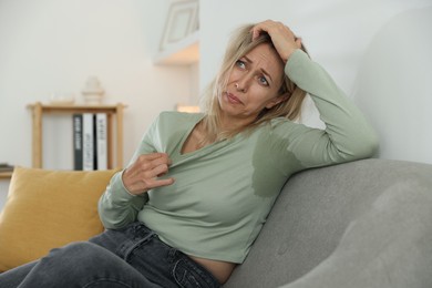 Photo of Menopause. Woman suffering from hot flash on sofa at home