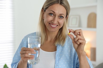 Menopause, hormone replacement therapy. Happy woman with glass of water and pill at home