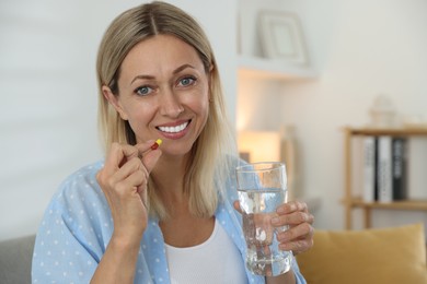 Menopause, hormone replacement therapy. Happy woman with glass of water and pill at home