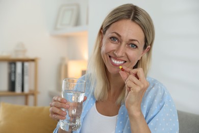 Menopause, hormone replacement therapy. Happy woman with glass of water and pill at home