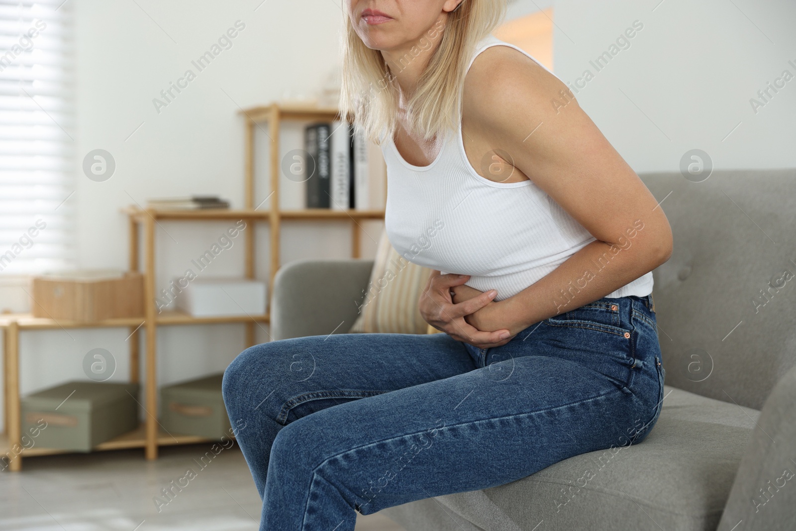 Photo of Menopause. Woman suffering from abdominal pain on sofa at home, closeup