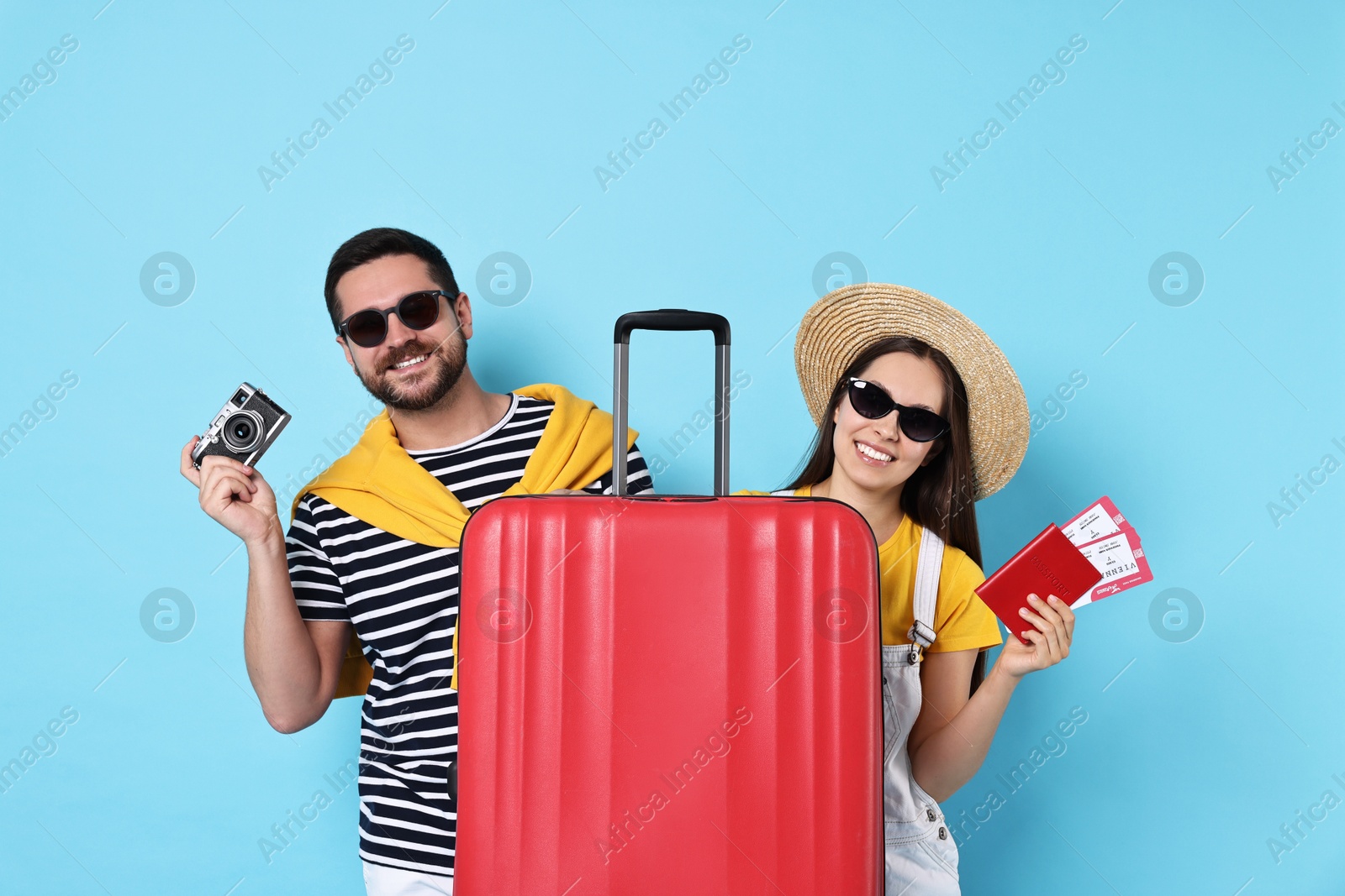 Photo of Happy couple with suitcase, passport, tickets and vintage camera on light blue background