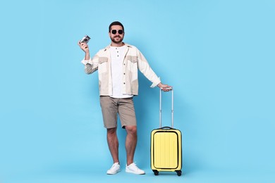 Photo of Happy man in sunglasses with vintage camera and suitcase on light blue background