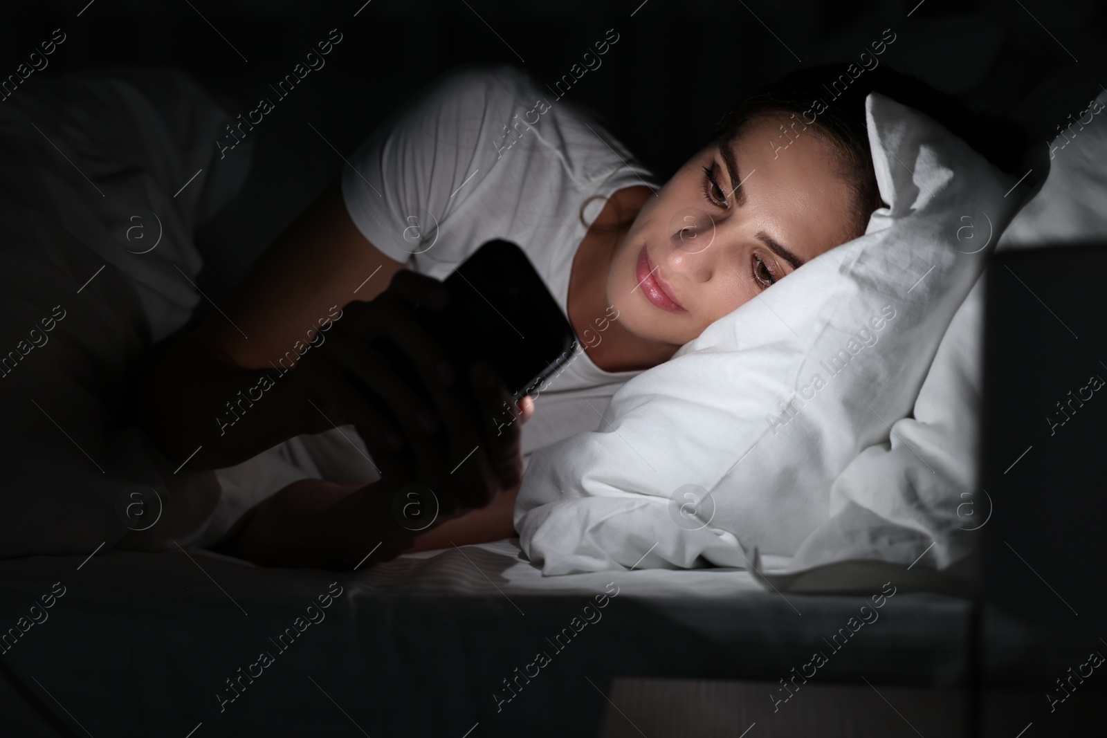 Photo of Bad habit. Young woman using smartphone in bed at night