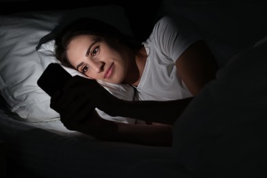 Photo of Bad habit. Young woman using smartphone in bed at night