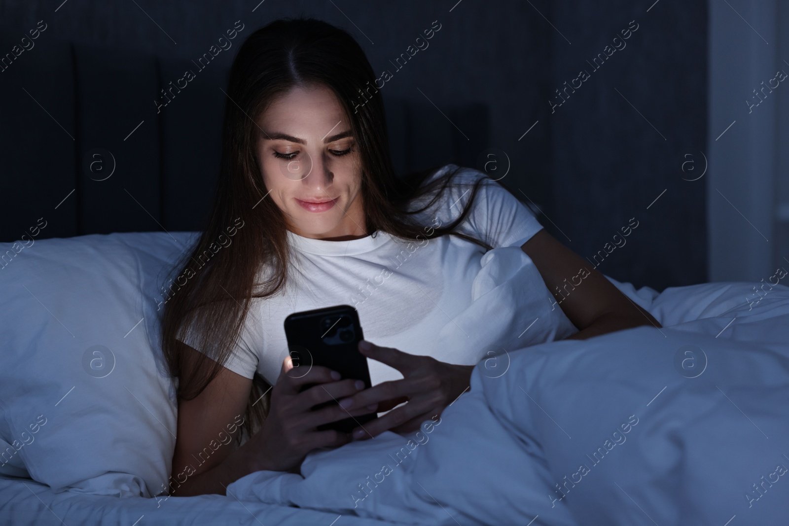 Photo of Bad habit. Young woman using smartphone in bed at night