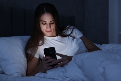 Photo of Bad habit. Young woman using smartphone in bed at night