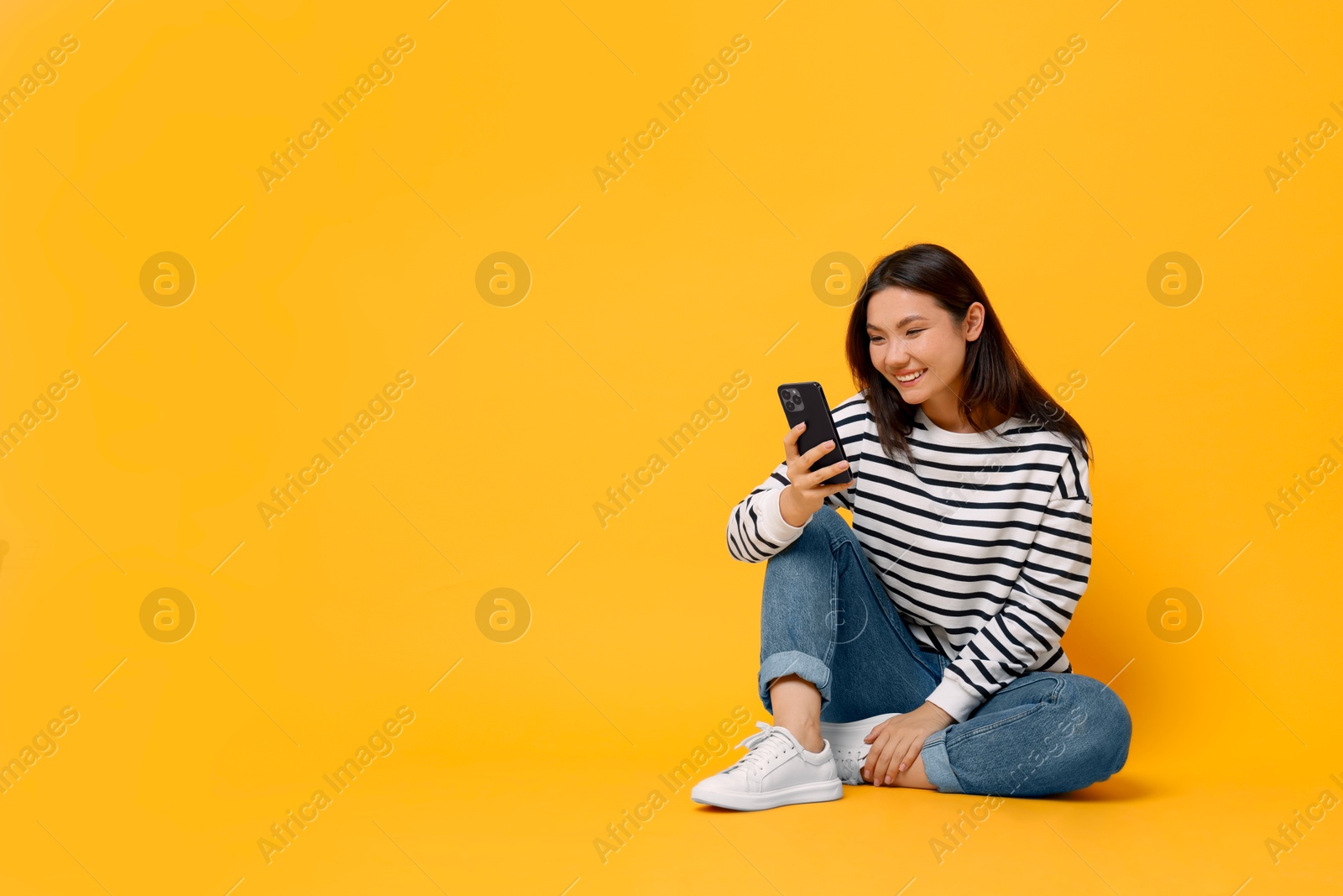 Photo of Smiling young woman using smartphone on yellow background. Space for text