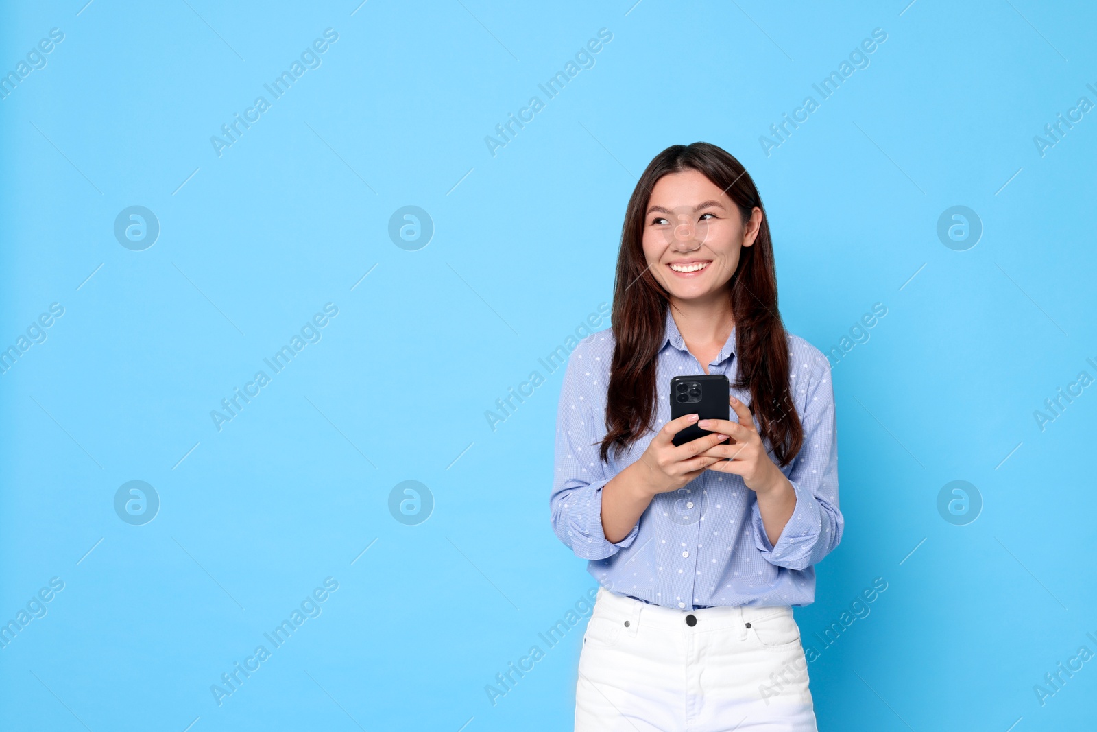 Photo of Smiling woman with smartphone on light blue background. Space for text