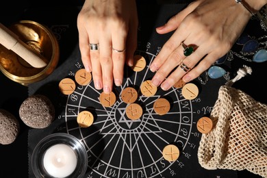 Woman with wooden runes at divination mat indoors, top view