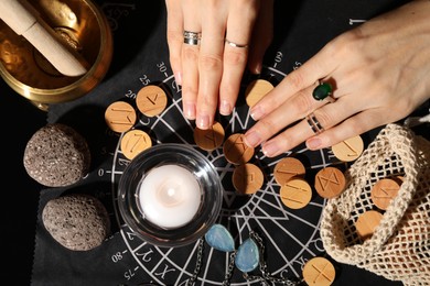 Woman with wooden runes at divination mat indoors, top view