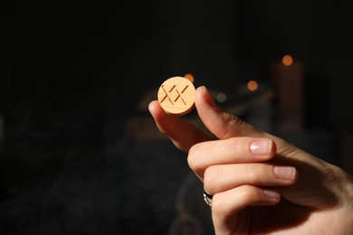 Photo of Woman with wooden rune Inguz on dark background, closeup. Space for text