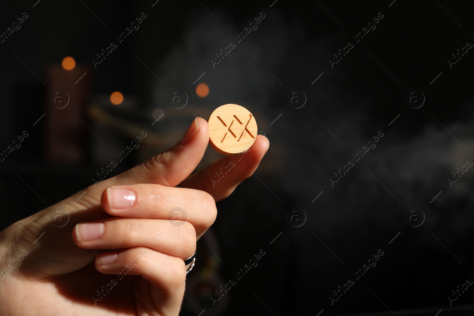 Photo of Woman with wooden rune Inguz on dark background, closeup. Space for text