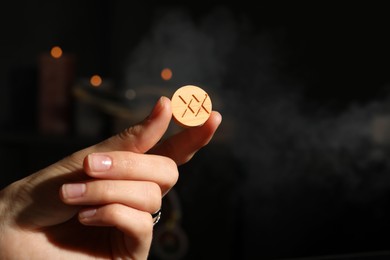 Woman with wooden rune Inguz on dark background, closeup. Space for text