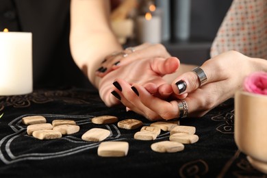 Photo of Fortuneteller reading woman's hand at table, closeup. Wooden runes on divination mat