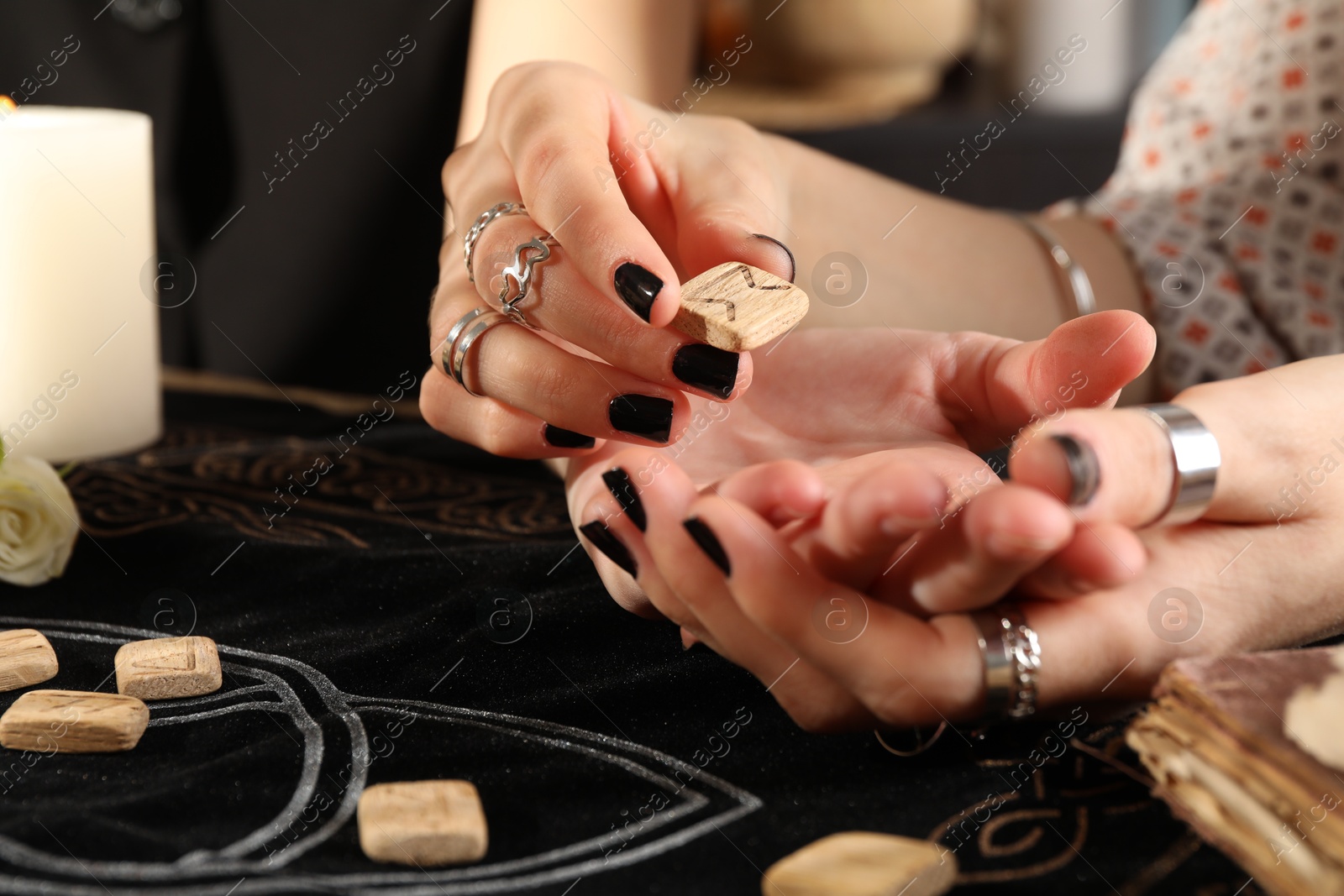 Photo of Fortuneteller reading woman's hand at table, closeup. Wooden runes on divination mat