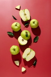 Photo of Fresh apples and green leaves on red background, flat lay