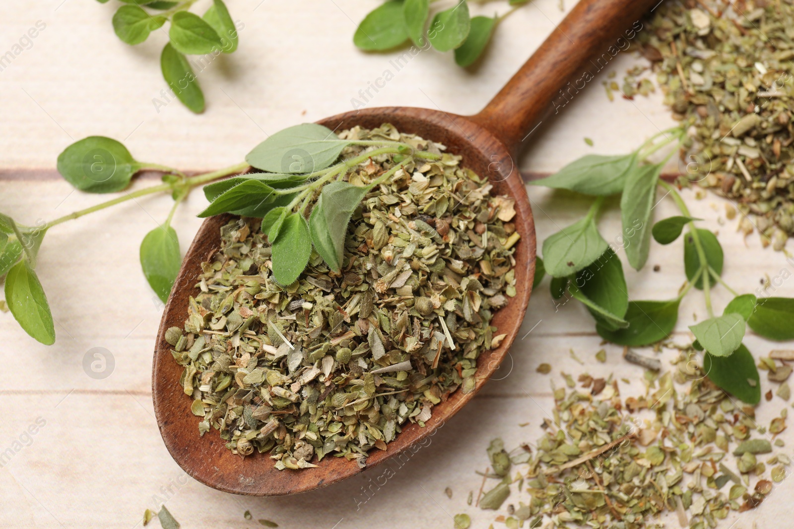 Photo of Dried oregano in spoon and green leaves on wooden table, closeup