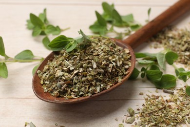 Photo of Dried oregano in spoon and green leaves on wooden table, closeup