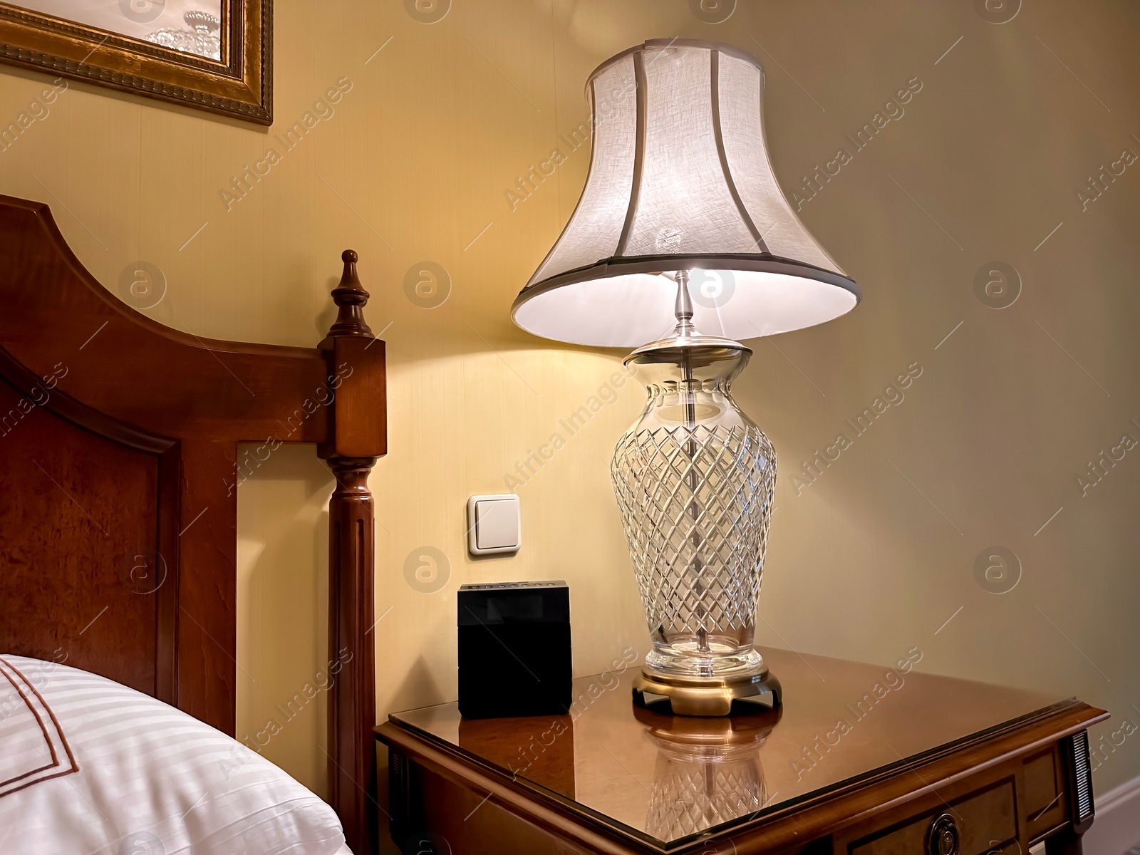 Photo of Lamp and electric clock on wooden bedside in luxury hotel